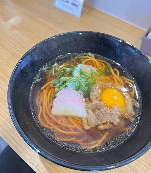 黒い器に盛られた辛麺に生卵と肉、ネギがトッピングされた料理