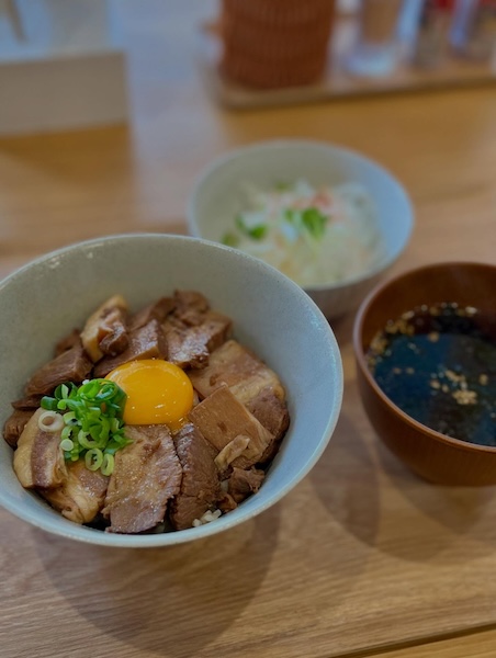 木製テーブルに並べられた煮豚丼セット。メインの煮豚丼、サラダの小鉢、海苔が浮かんだスープの3点が配置されている