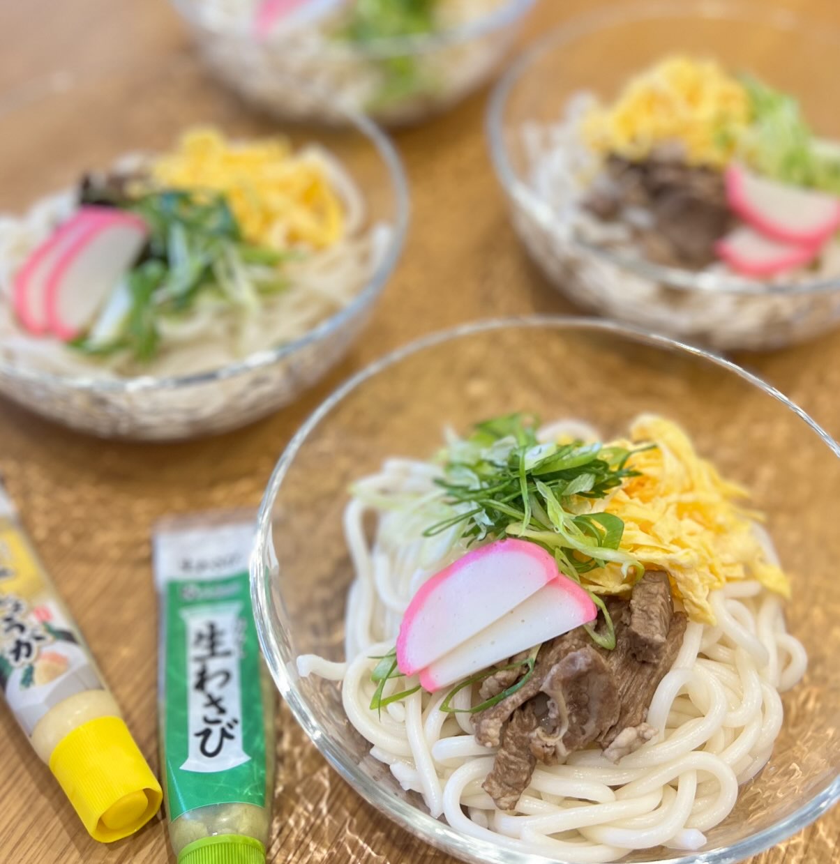 ガラスの器に盛られた冷やしうどん。煮込んだ牛肉・錦糸卵・かまぼこ・ねぎのトッピング
